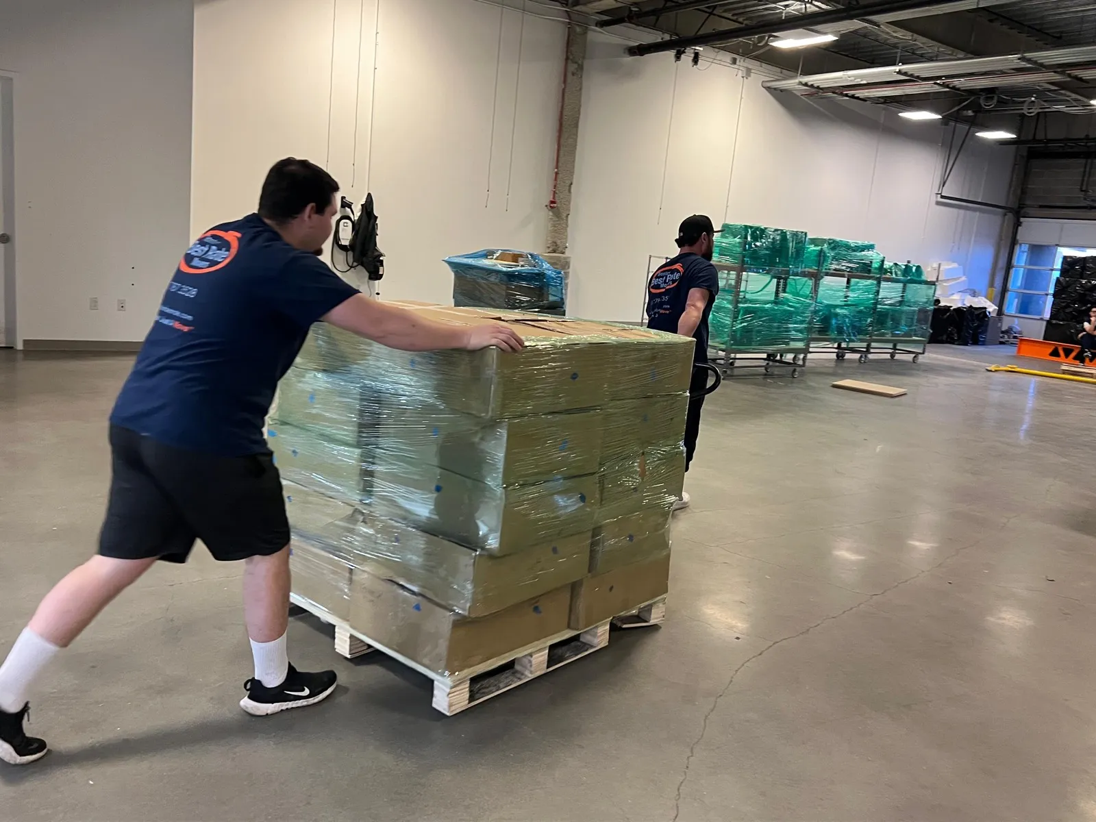 Two BBRM crew members pushing wrapped pallet in commercial space